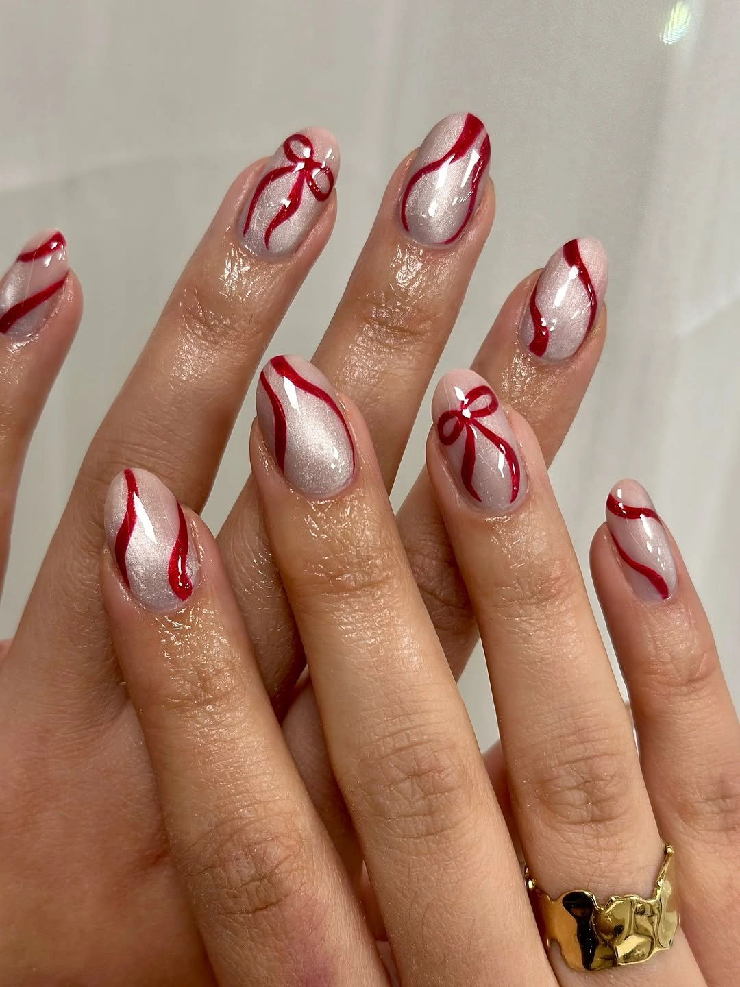 Pale shimmer nails with curved red lines and red bows