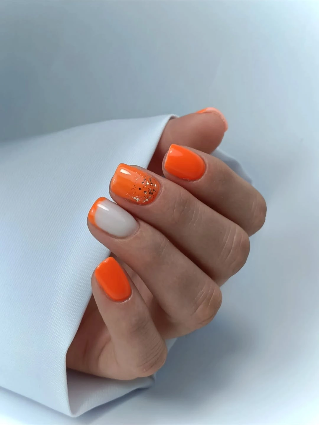 Orange short nails with white and speckled accent nails