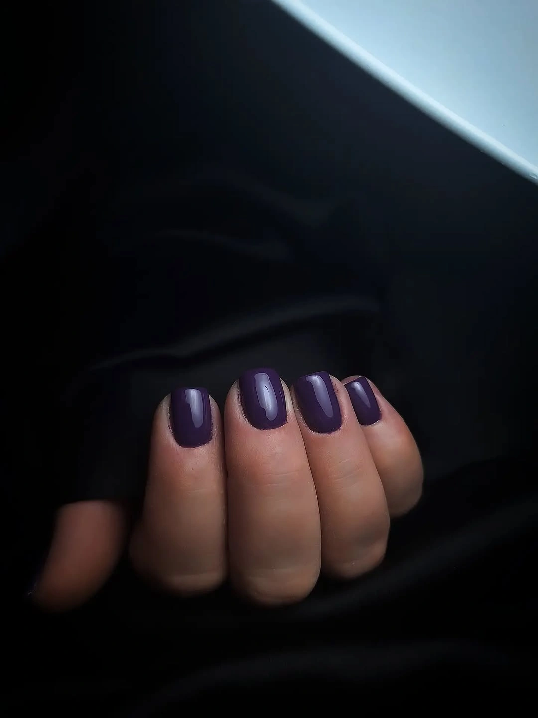 Dark plum glossy short square nails against black fabric