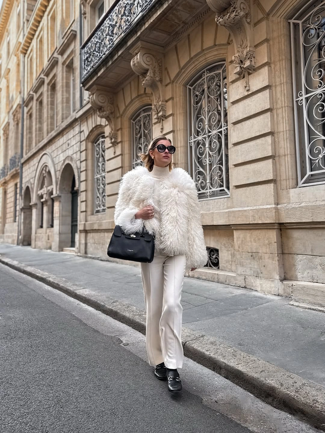 White fuzzy jacket and trousers with black loafers and bag
