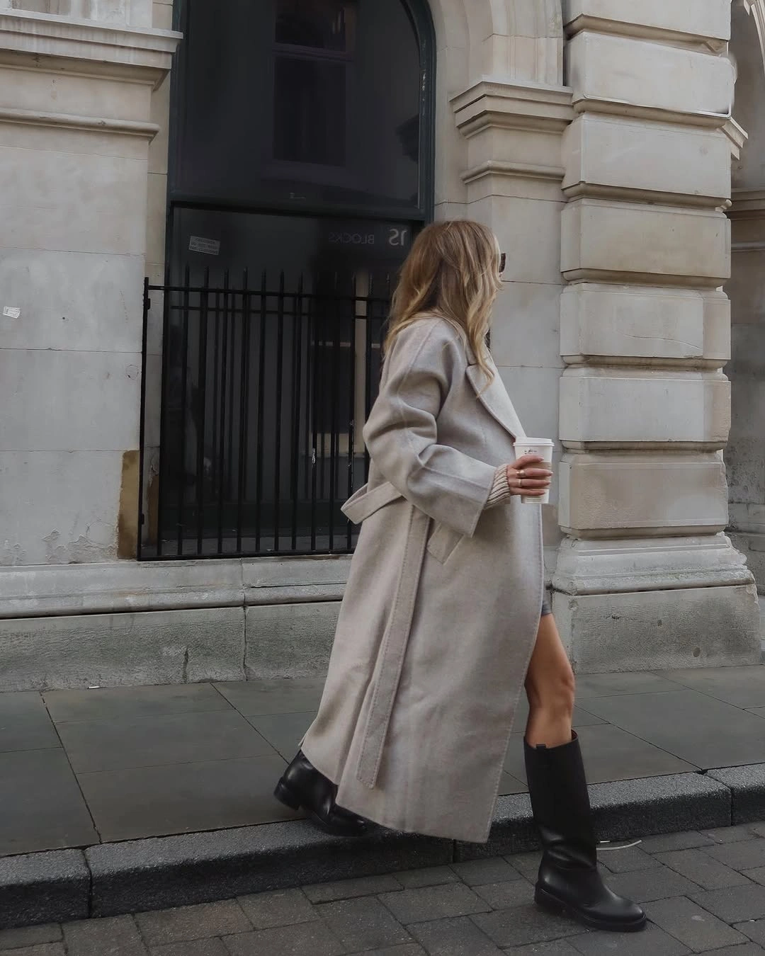 Beige-gray long belted coat with black tall boots