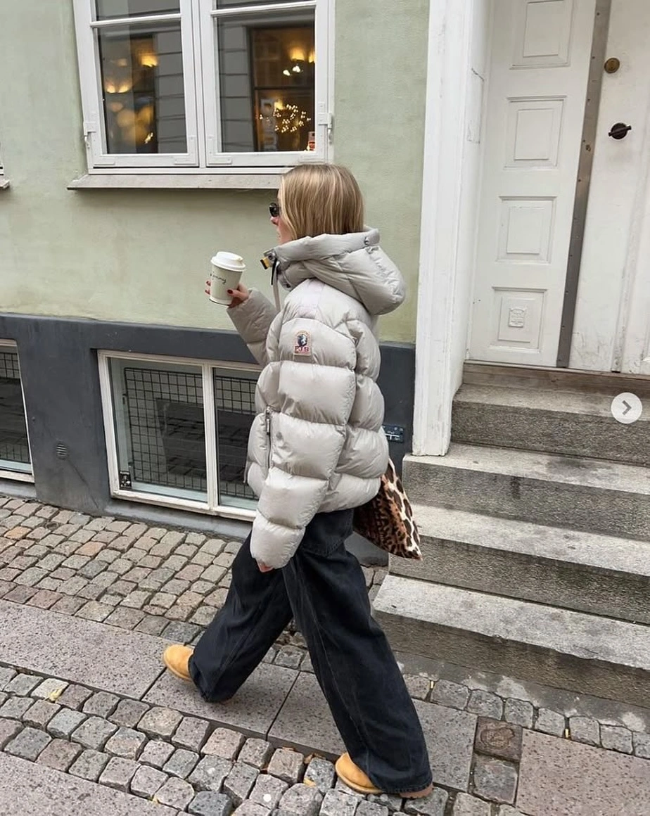 Pale hooded padded jacket with dark wide pants and tan shoes