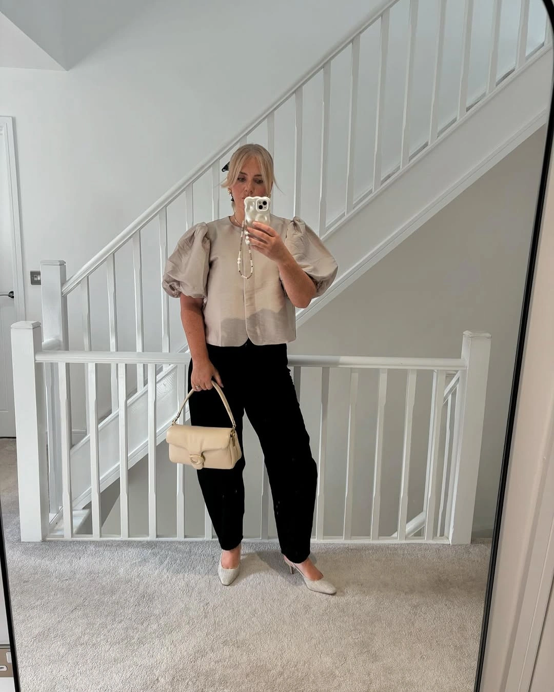 Beige puff-sleeve top with black trousers and cream handbag