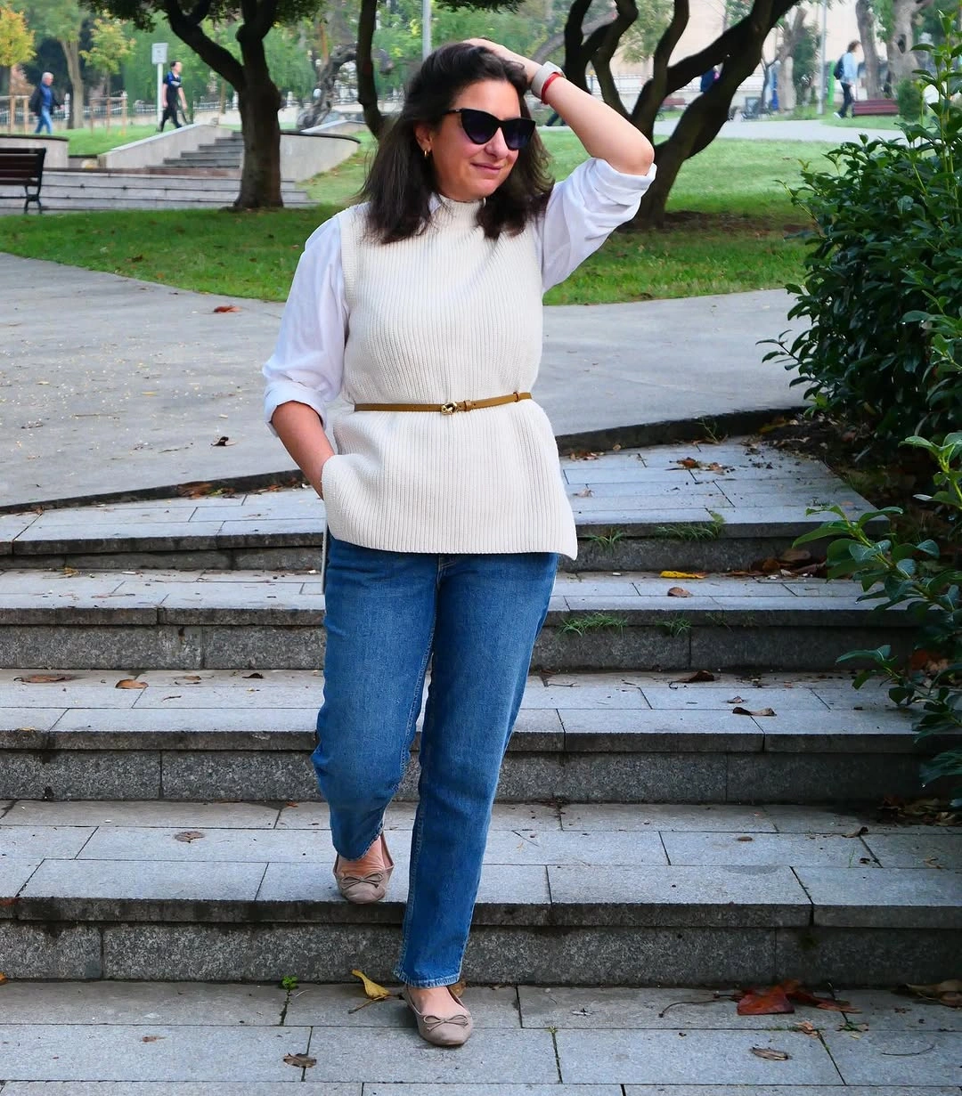 Cream knit vest over white shirt sleeves and blue jeans