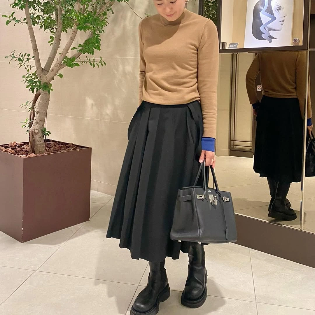 Tan sweater with black pleated skirt and lug-sole boots