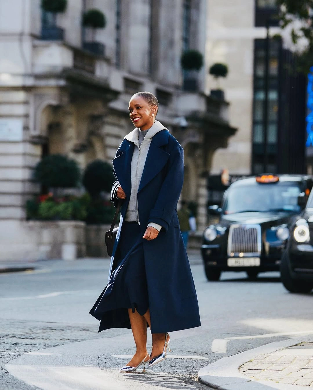 Long navy coat with pale high-neck top and metallic heels