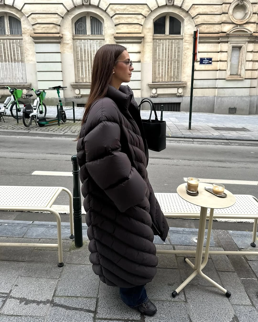 Long dark puffer coat with jeans, boots, and held handbag