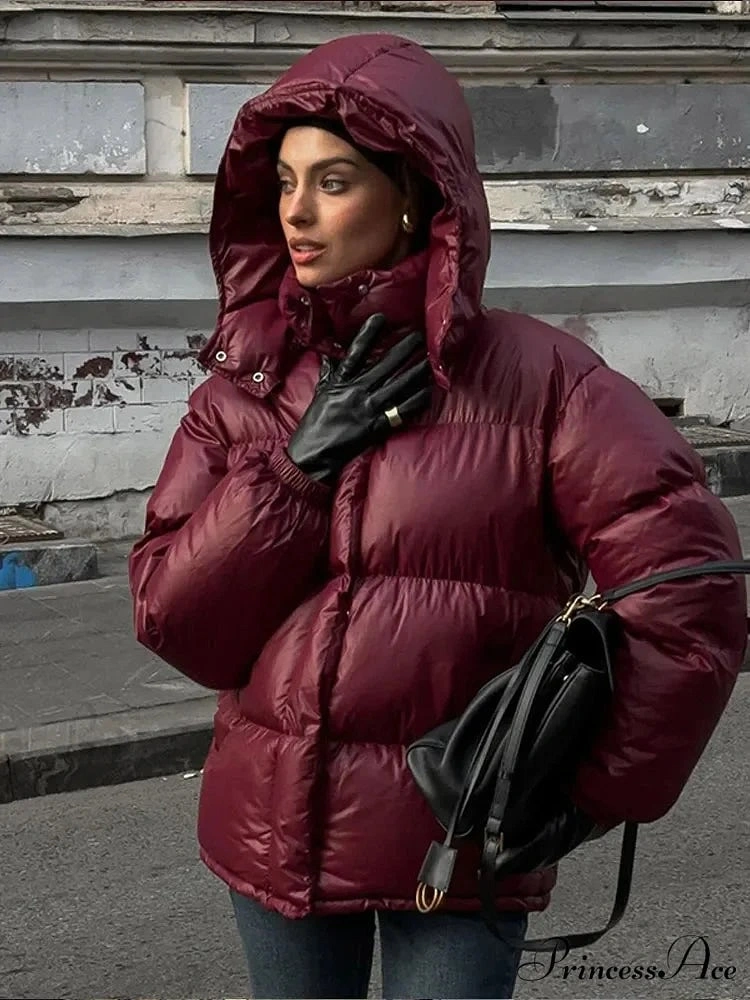 Glossy-looking burgundy hooded puffer with black gloves and bag