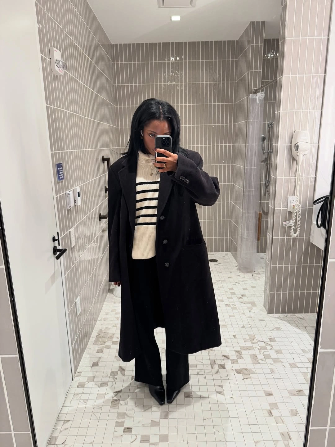 Long dark coat over striped sweater and wide black trousers