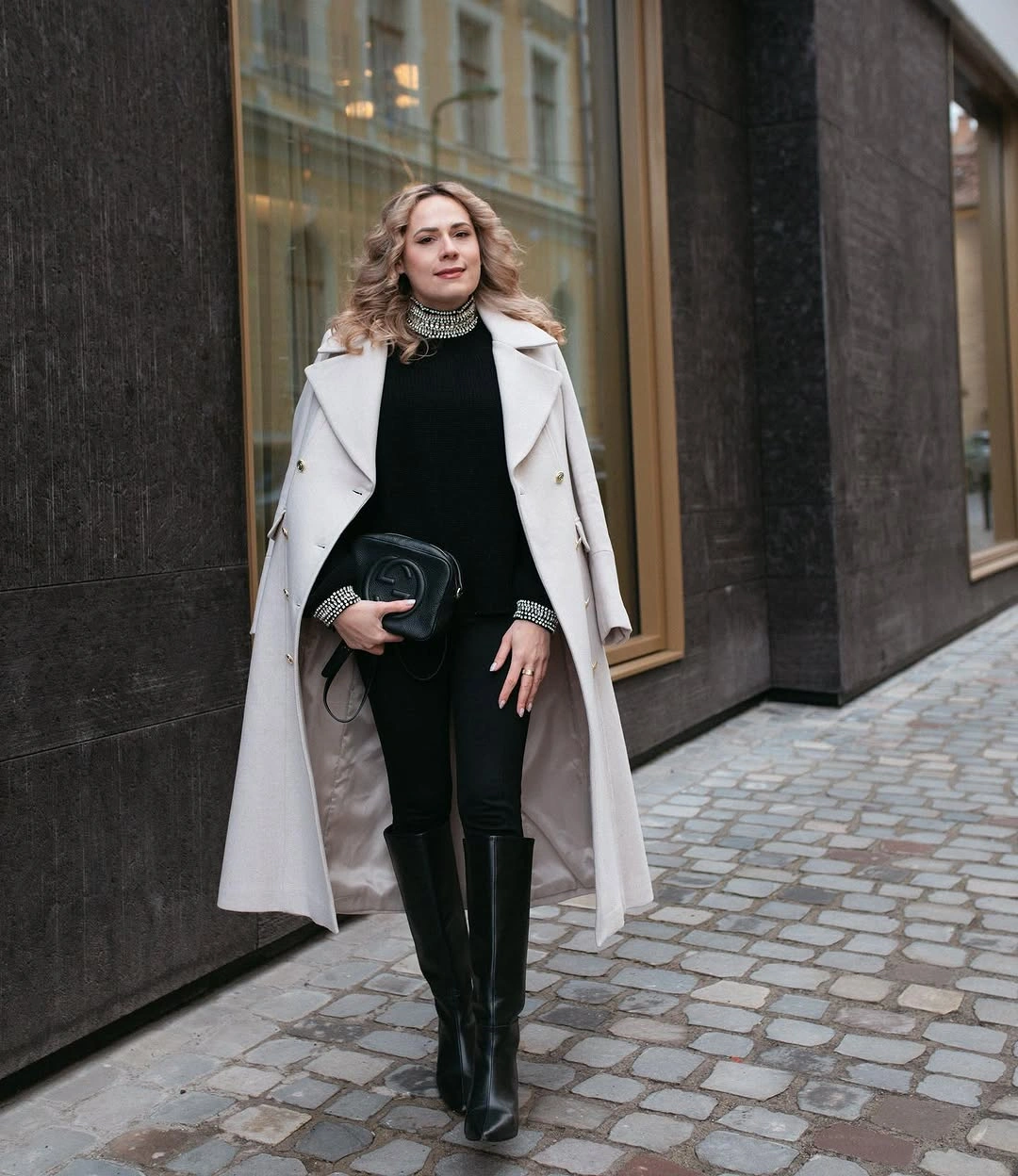 Pale long coat over black outfit with tall boots
