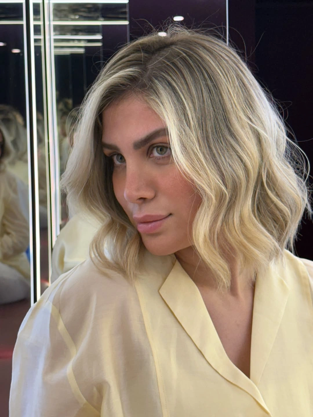Short creamy-blonde wavy bob with darker crown depth and side part