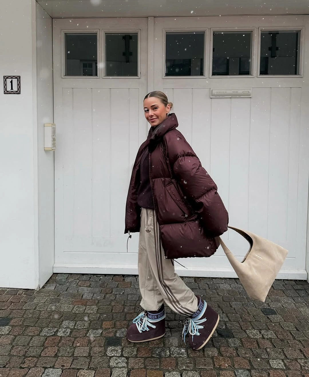 Burgundy puffer jacket with relaxed beige trousers, matching sneakers, and cream tote