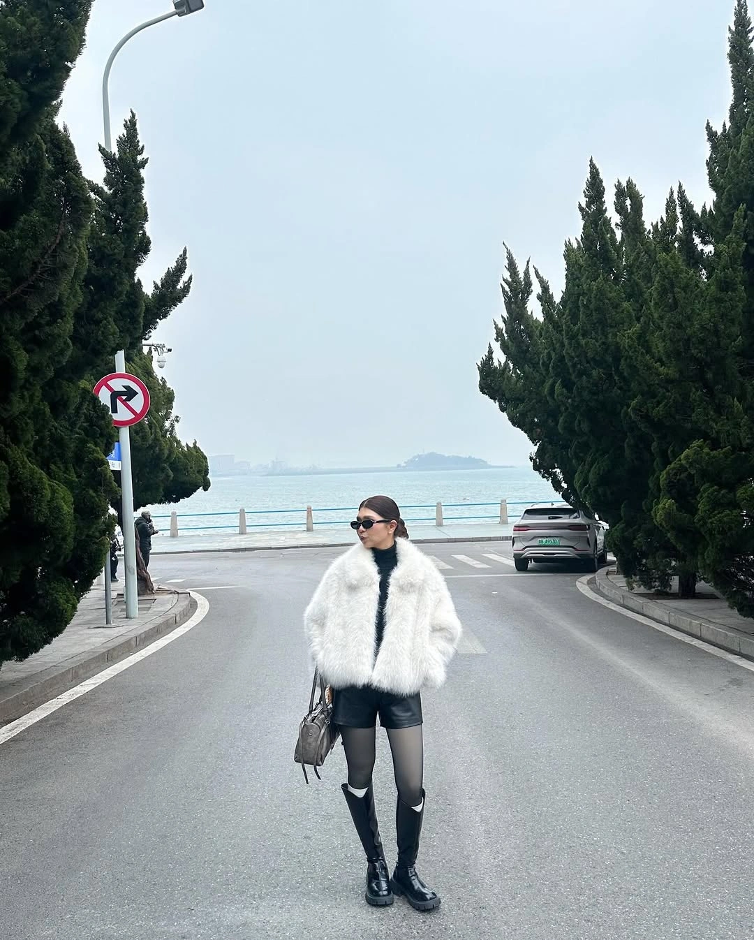 Short white textured jacket over black dress, tights, and knee-high boots