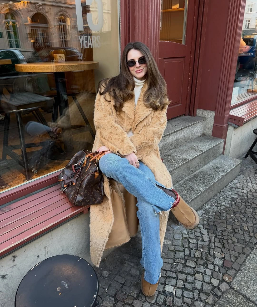 Tan textured long coat with white turtleneck, blue jeans, and brown boots