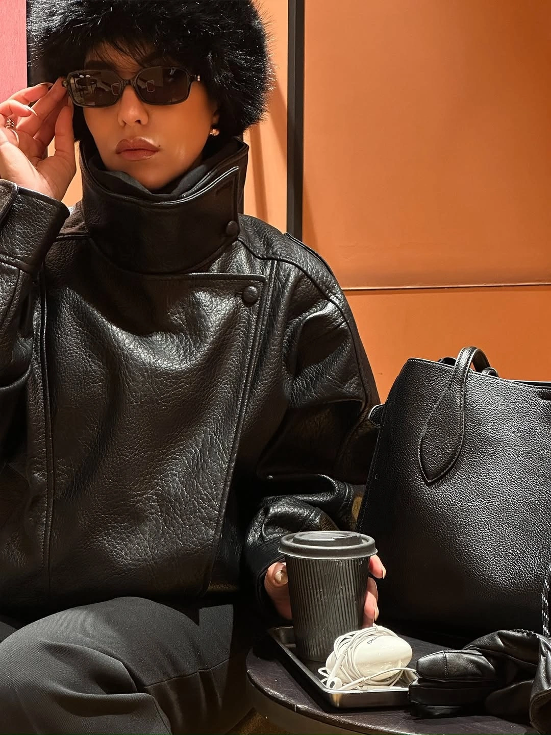 Glossy-looking black jacket with fuzzy-textured hat and black tote