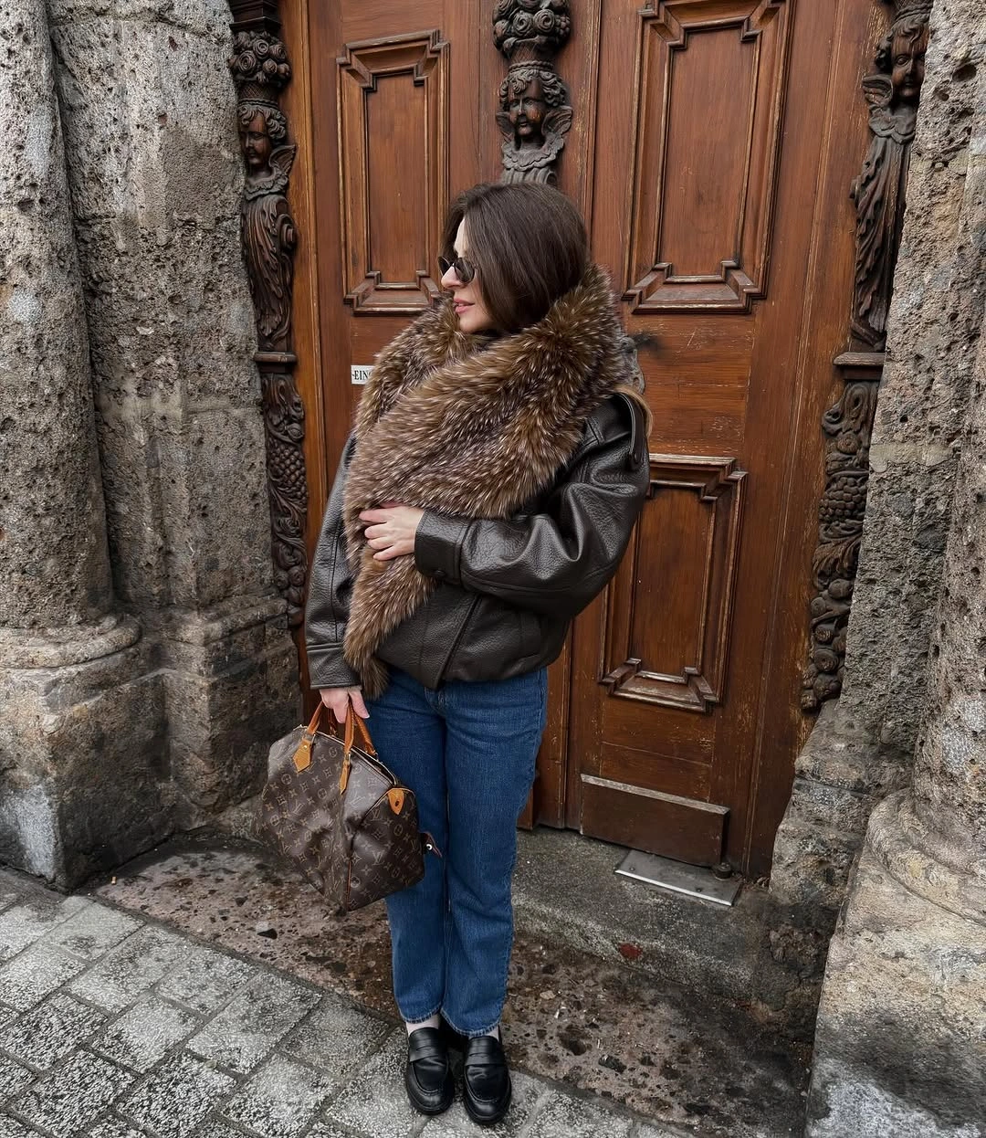 Brown shaggy-looking wrap over glossy-looking jacket with jeans and loafers