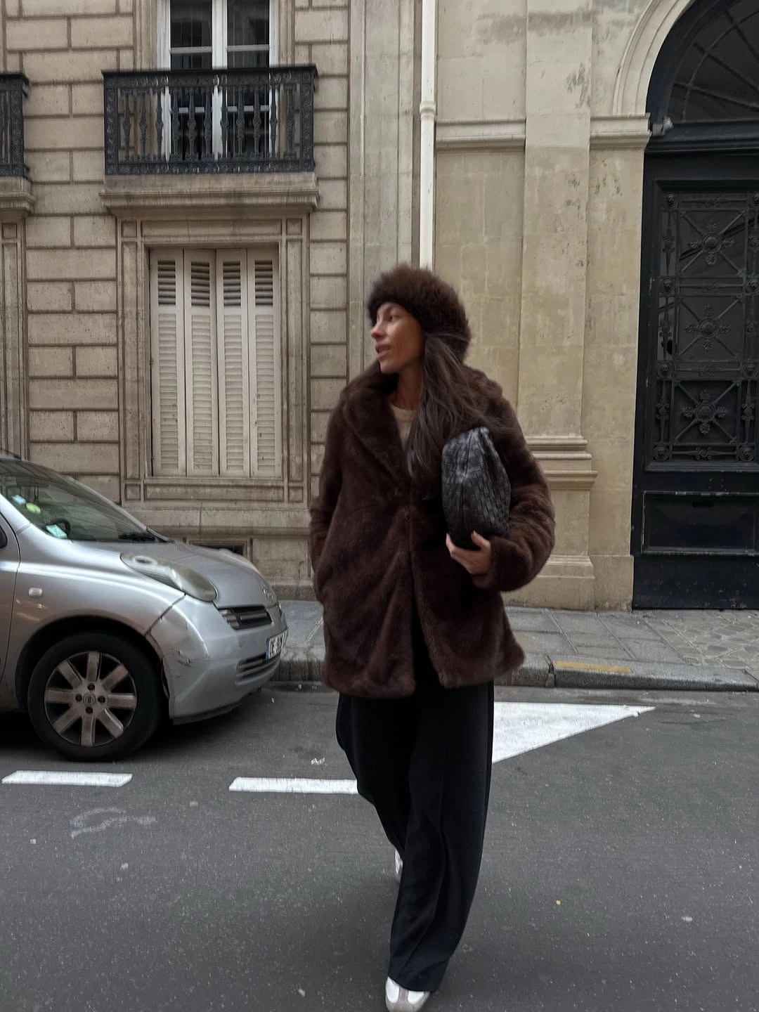 Dark brown fuzzy-textured coat black trousers patterned clutch and brown hat