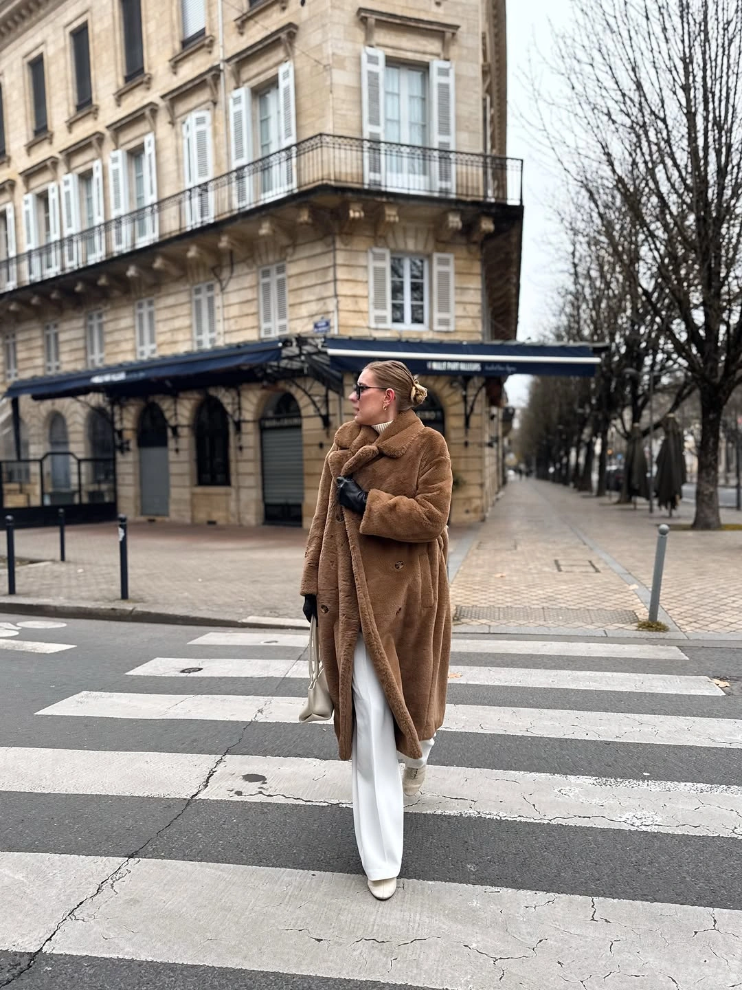 Long brown fuzzy-textured coat with white trousers and pale boots