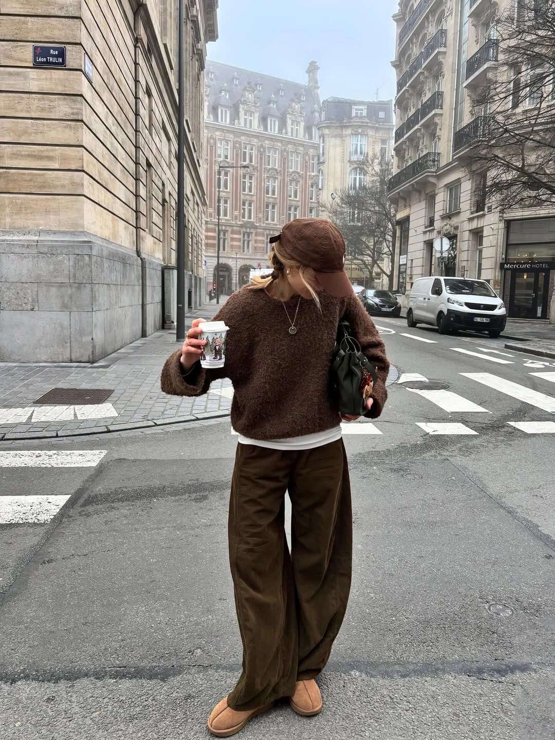 Brown sweater dark trousers cap tan shoes and green bag