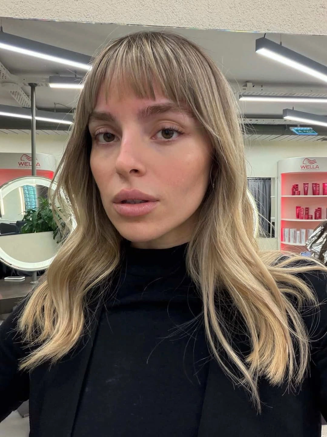 Shoulder length blonde waves with full bangs and darker lowlights