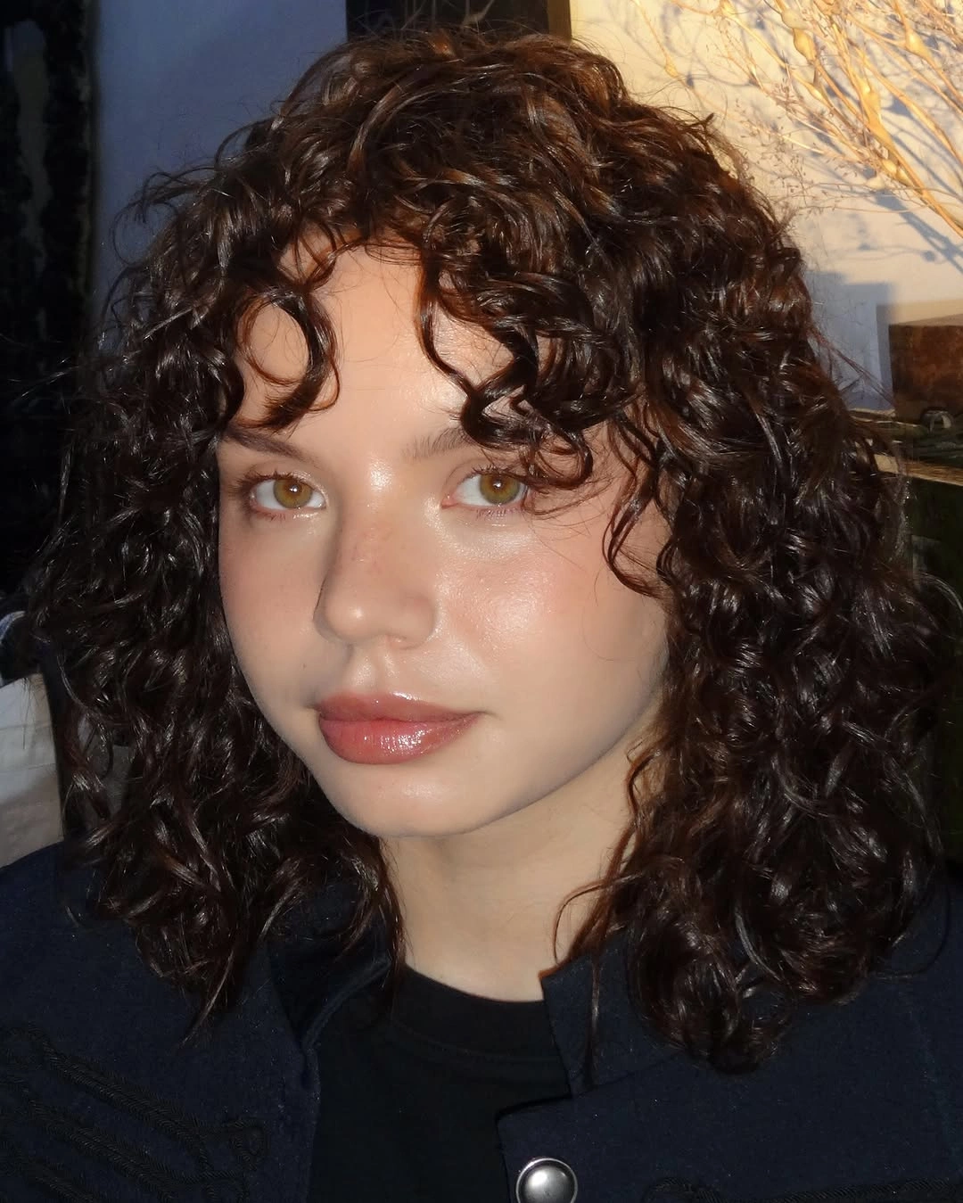Dark shoulder-length curly haircut with shorter fringe curls