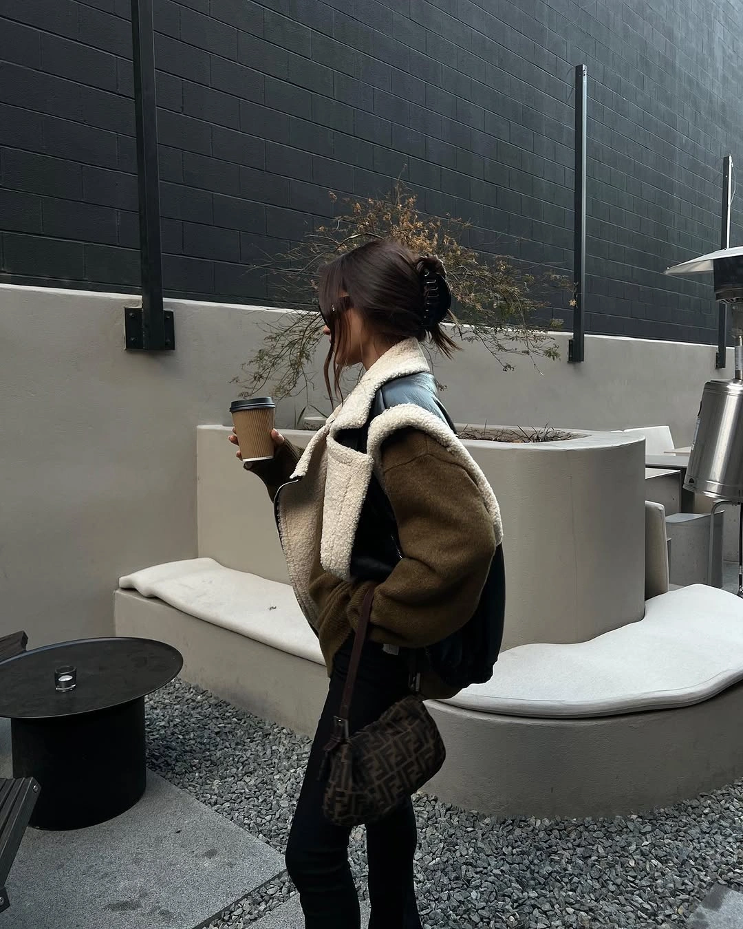 Brown jacket with pale collar, black pants, and dark bags