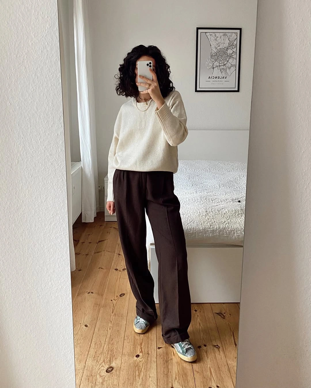 Cream sweater with dark brown trousers and gray sneakers