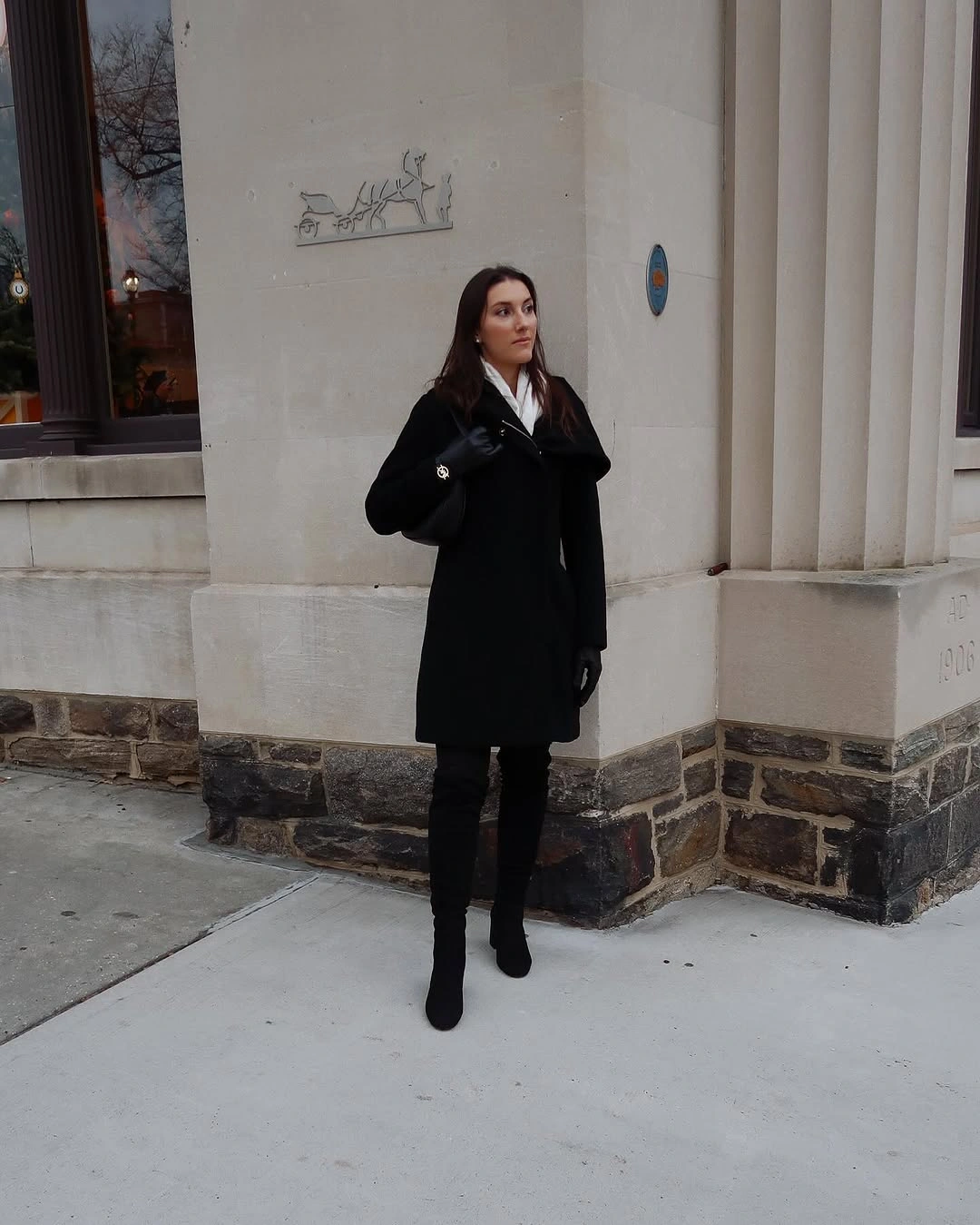 Black knee-length coat with dark boots and shoulder bag