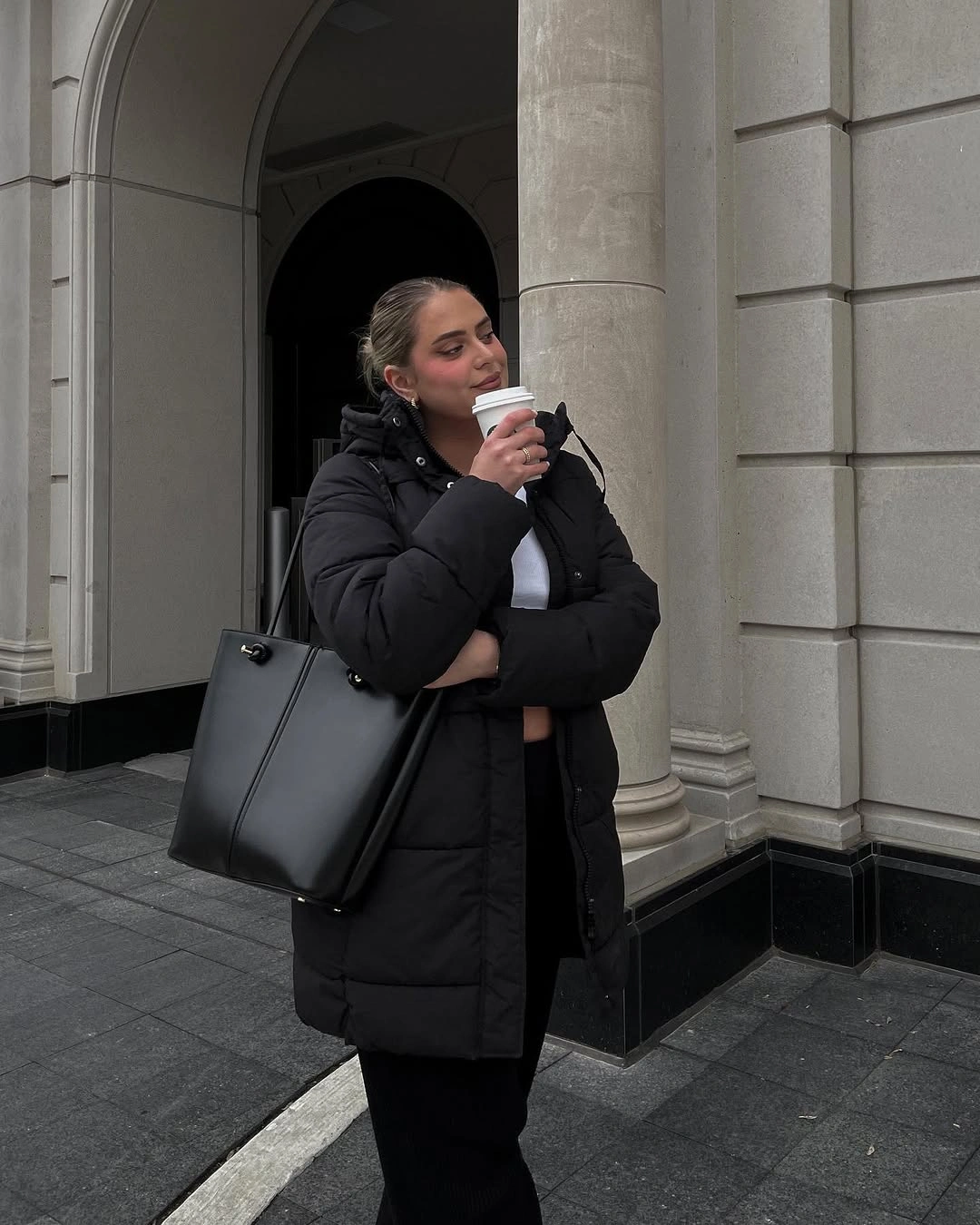 Long black padded coat with white top and black tote