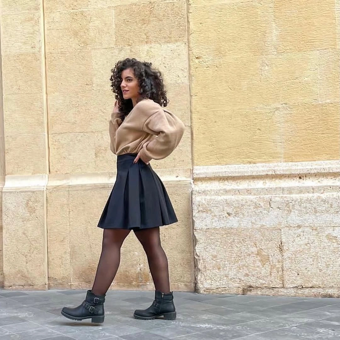 Beige sweater with black skirt, tights, and boots