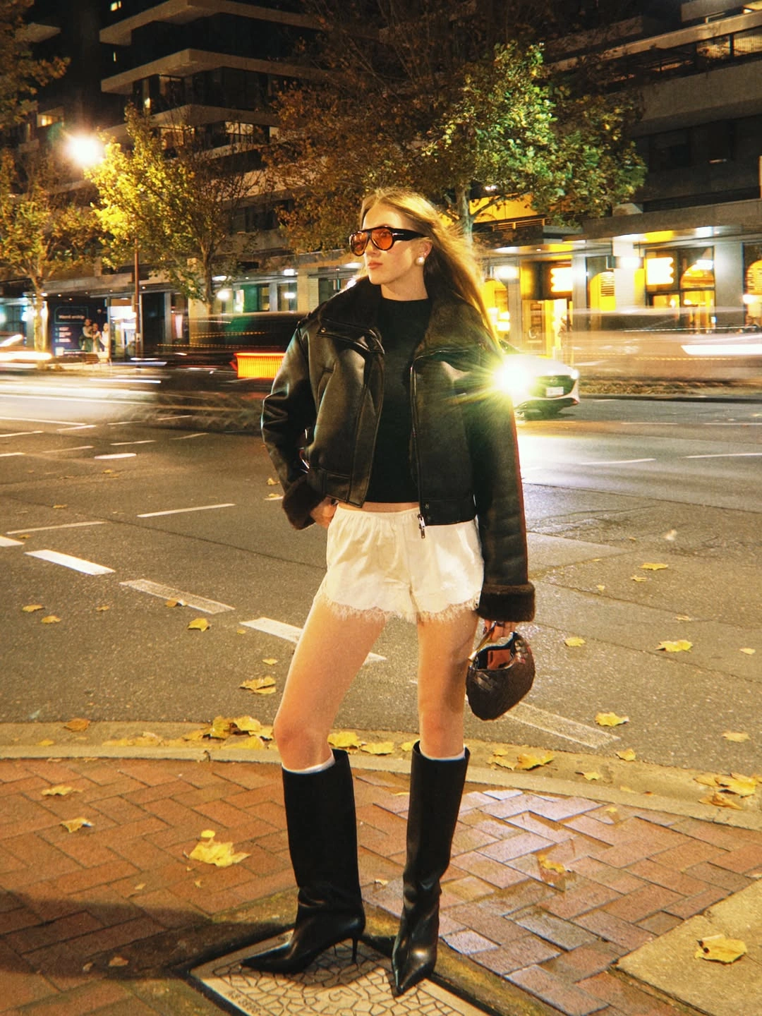 Black leather jacket with cream shorts and tall black boots