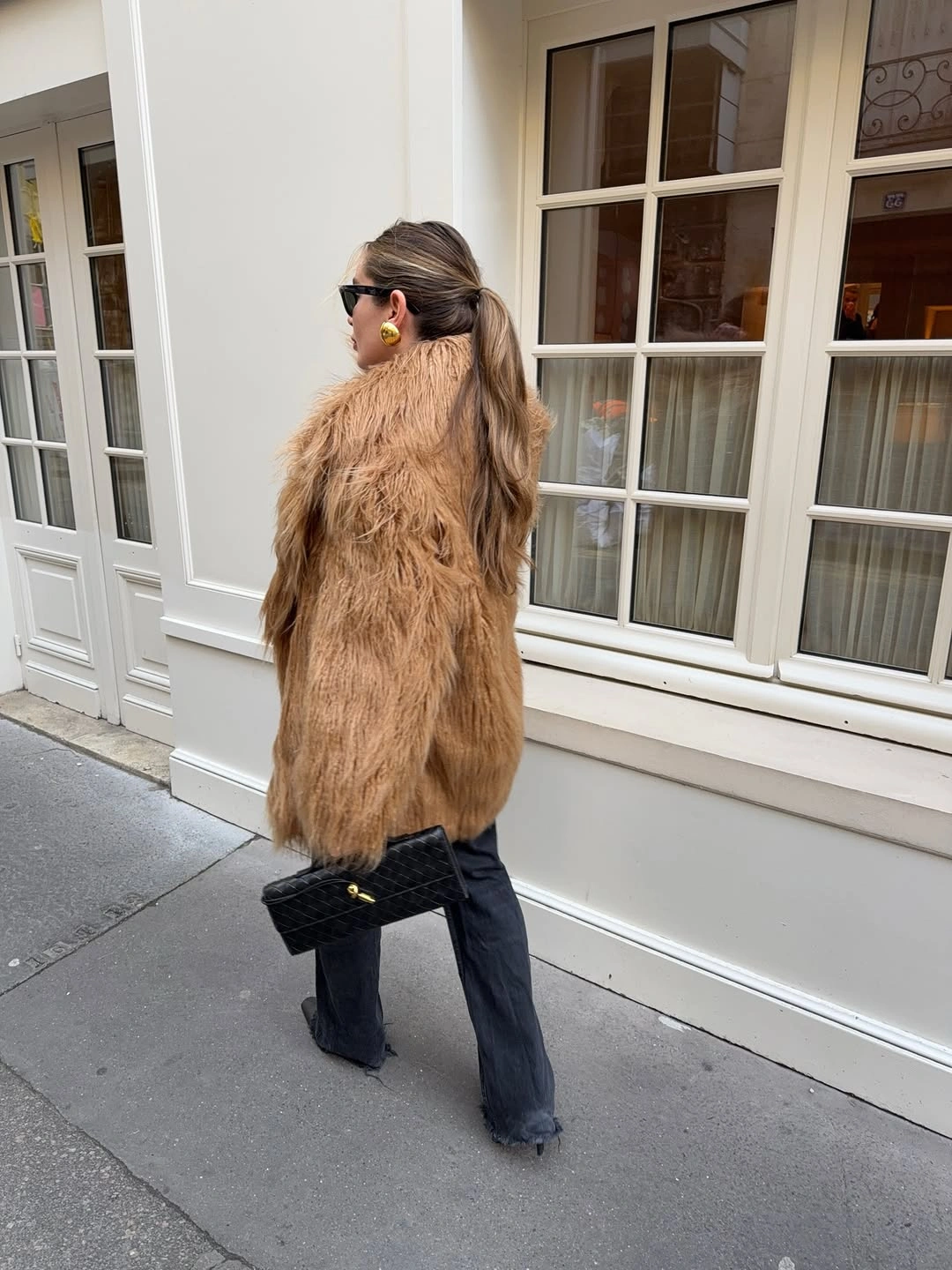 Tan shaggy coat with black flared pants and black bag