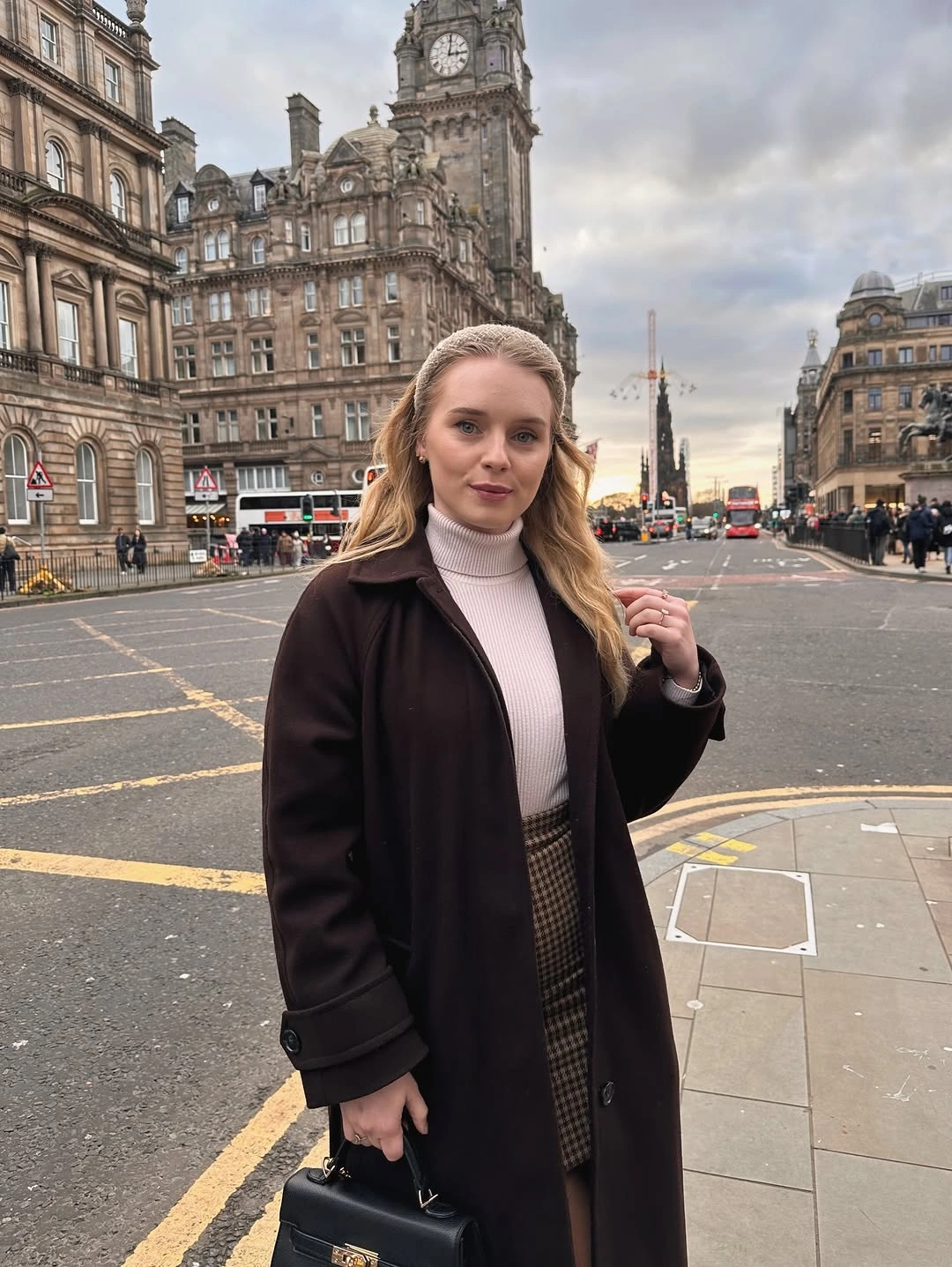 Dark coat with pale turtleneck, checked skirt and black handbag