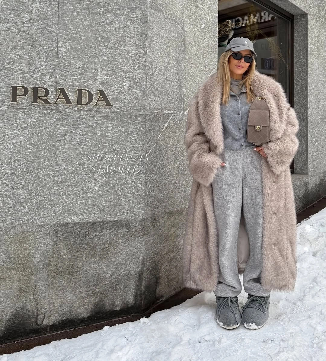 Long pale plush coat over gray sweats with sneakers and cap