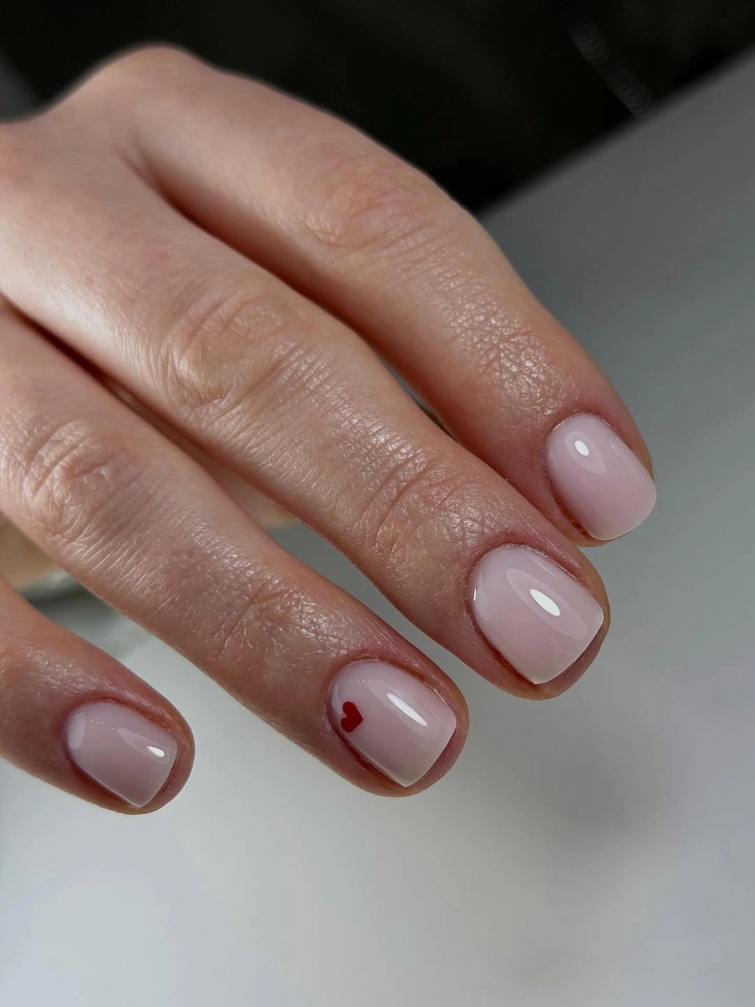 Very short pale pink nails with one tiny red heart