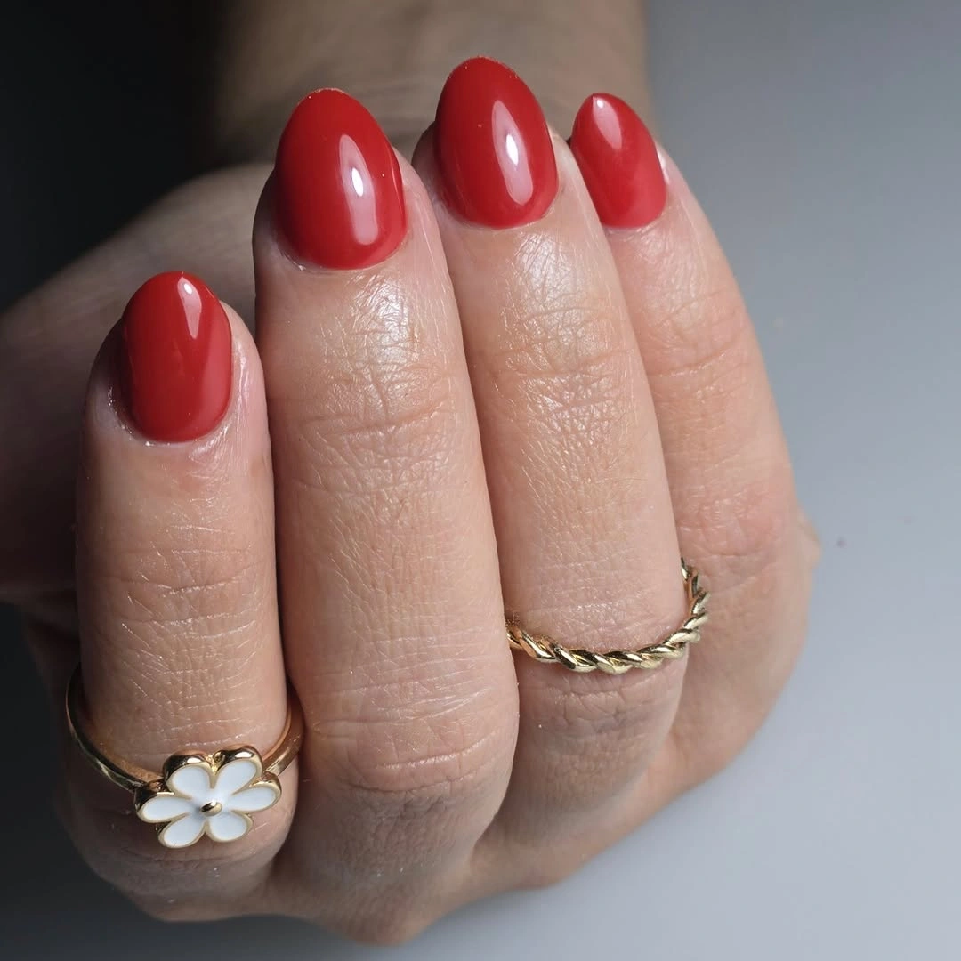 Glossy warm red short rounded nails with gold rings