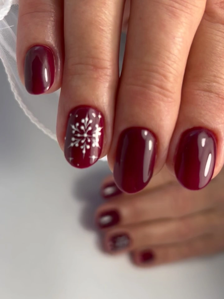 Deep burgundy short nails with one white snowflake accent