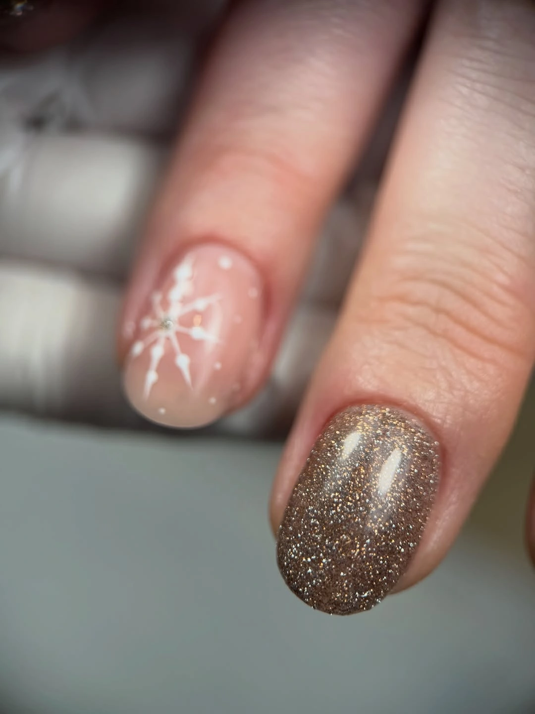Short rounded nails with gold glitter and white snowflake art