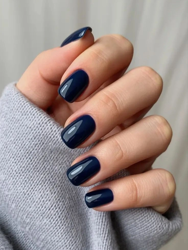 Glossy navy short squoval nails beside a pale gray sleeve