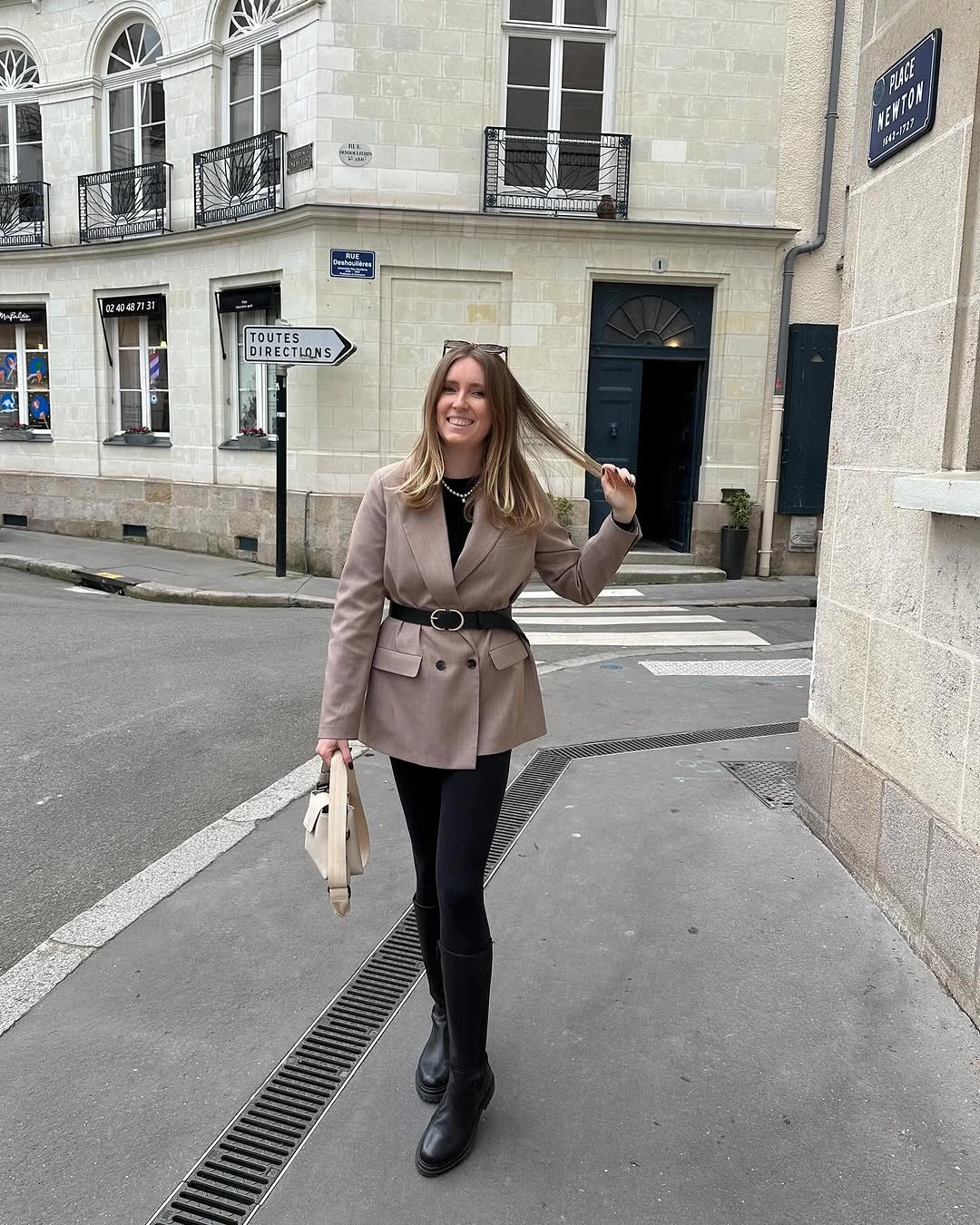 Taupe belted double-breasted blazer, black legwear, tall boots, and cream handbag