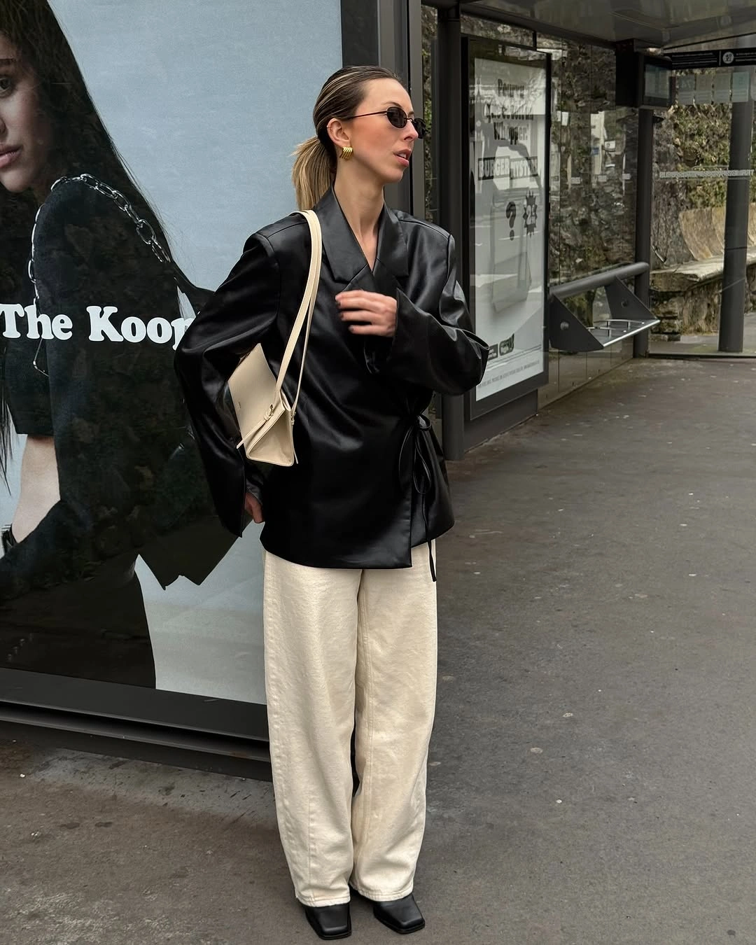 Oversized black leather-look jacket, wide ivory trousers, pale bag, and dark shoes