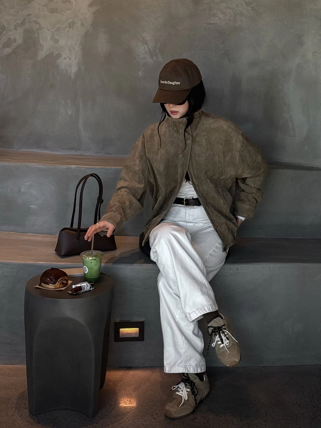 Olive-brown oversized jacket, brown baseball cap, white trousers, and neutral sneakers