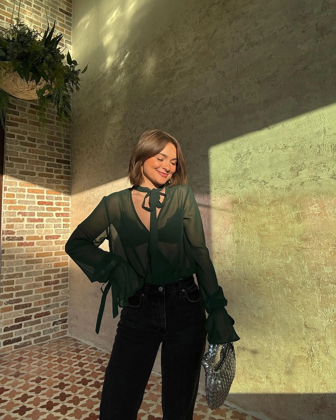 Sheer dark green blouse with neck tie, black jeans, and patterned bag