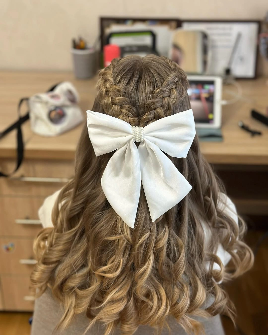 Two back braids meet beneath a large white bow