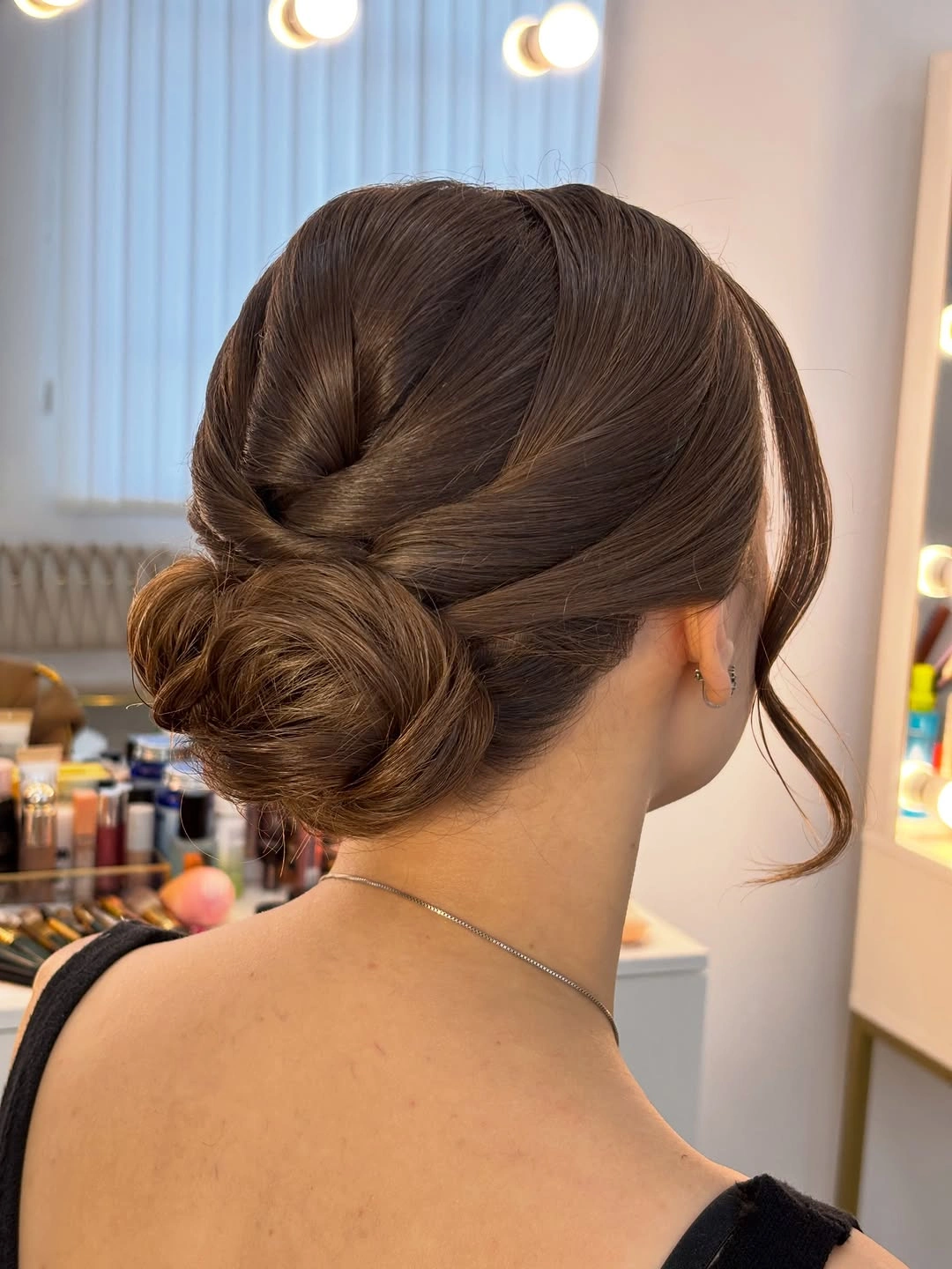 Low brown bun with twisted sections and face-framing strand