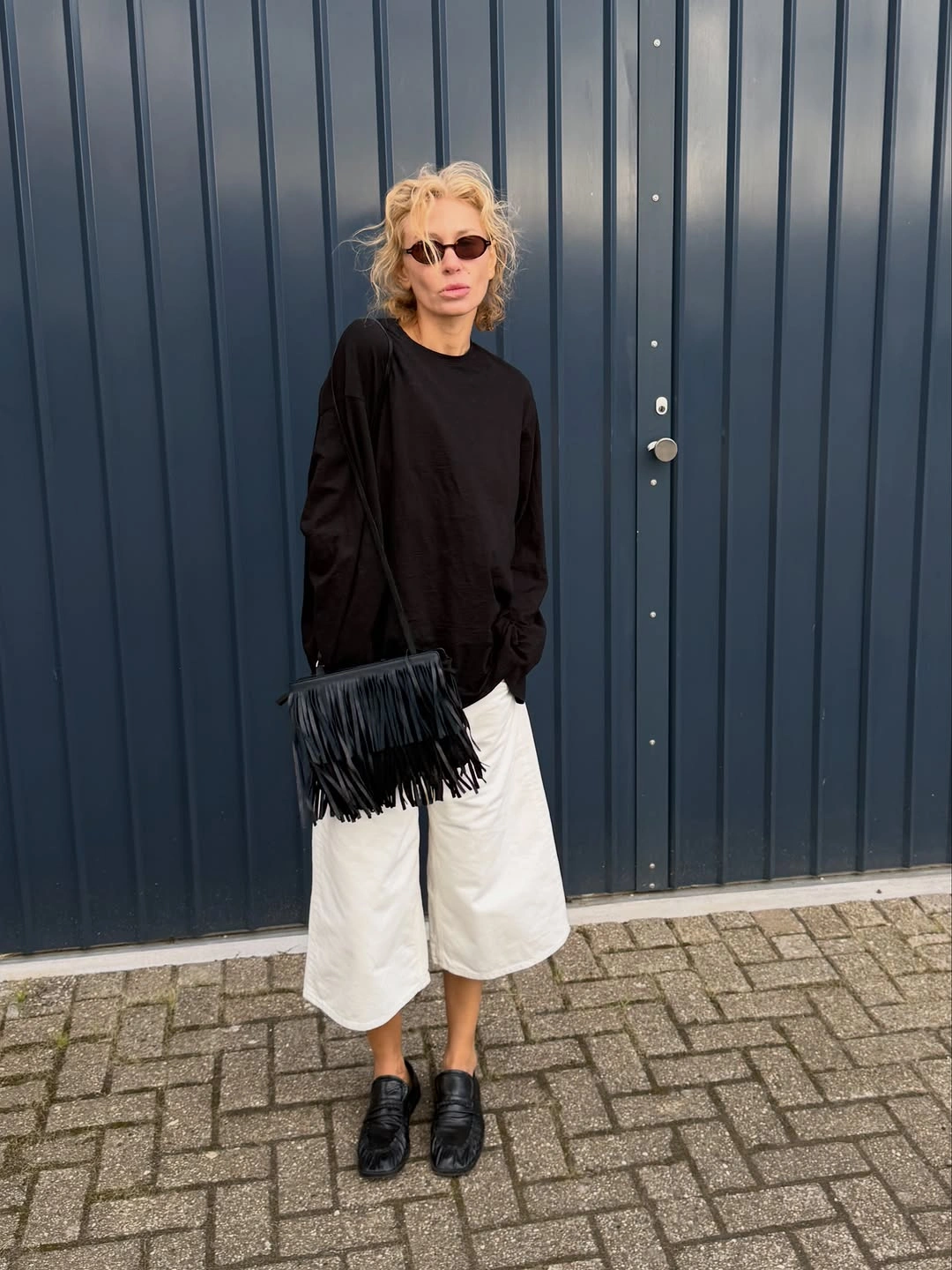 Oversized black long-sleeved top with white knee-length shorts and black loafers