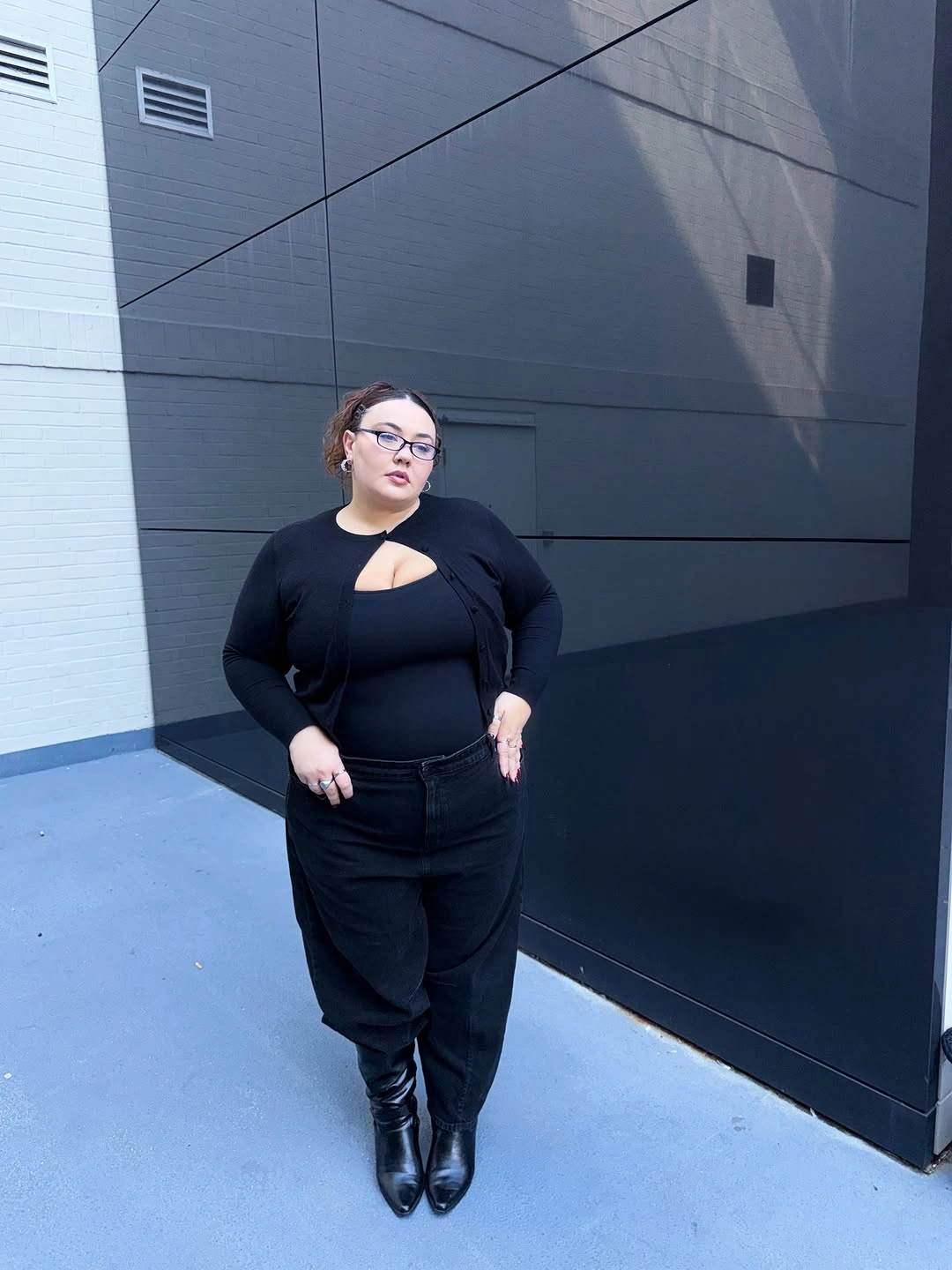 Black fitted top with asymmetrical chest cutout dark trousers and pointed boots