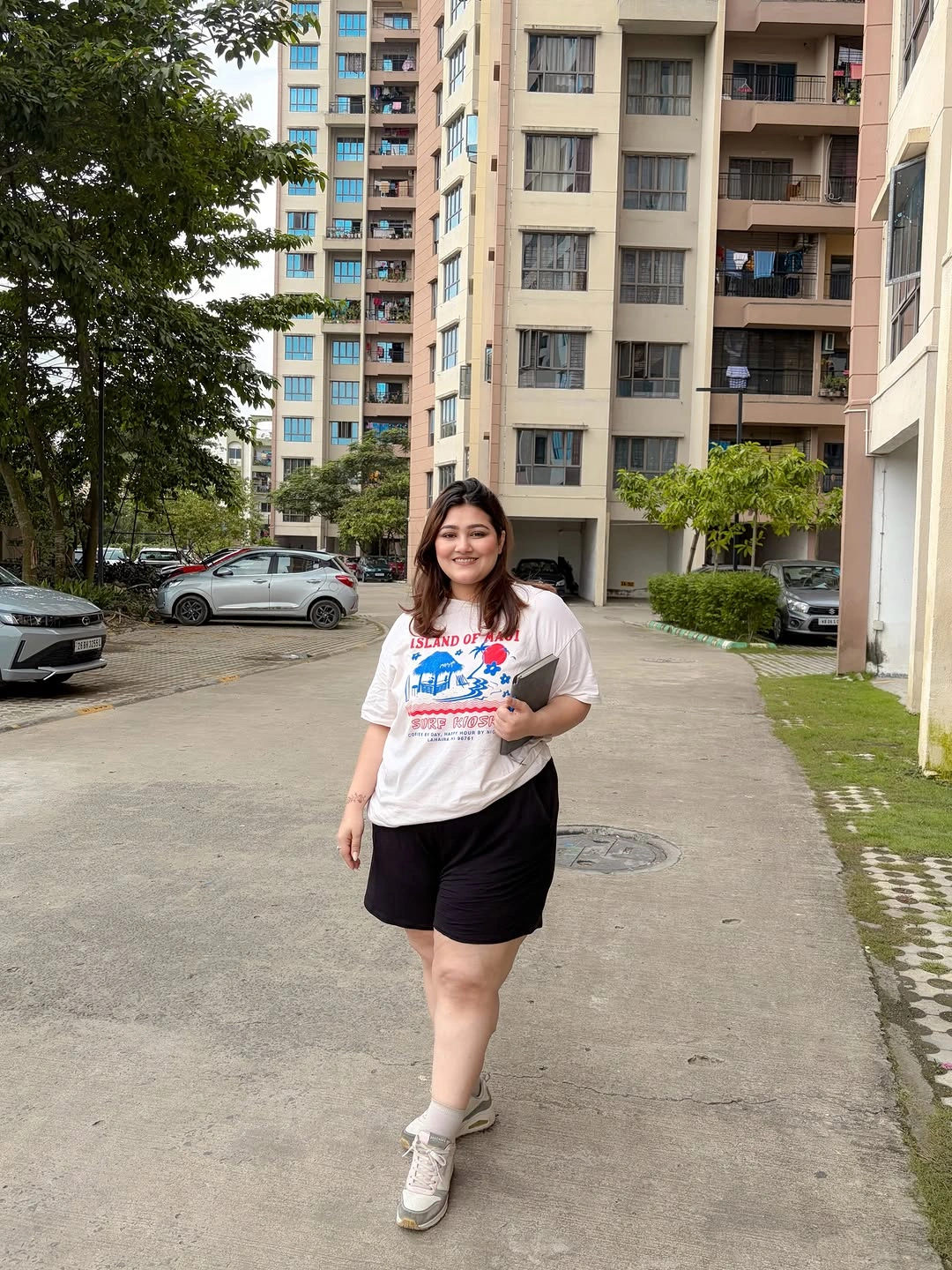 Loose white graphic T-shirt black knee-length shorts pale sneakers and gray bag