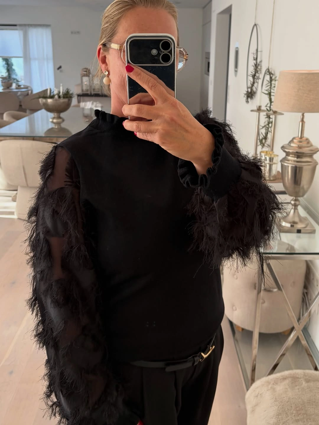 Black high-neck top with voluminous feather-like sleeves dark trousers and slim belt