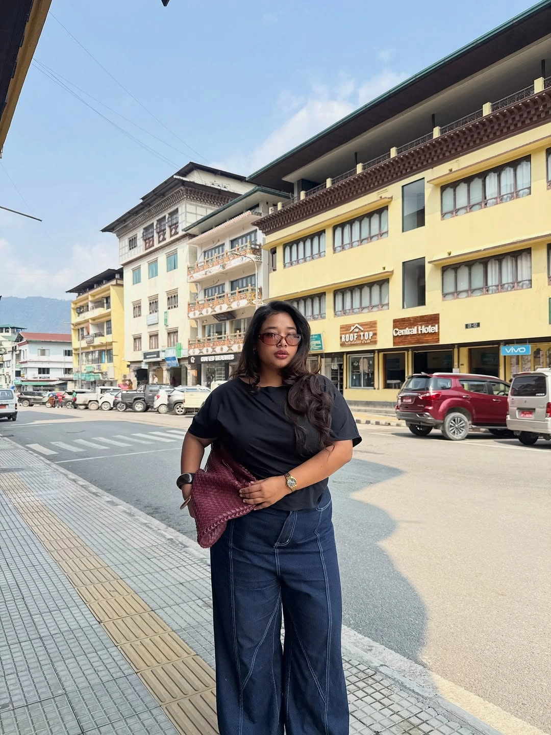Black short-sleeved top dark wide-leg jeans burgundy clutch and glasses